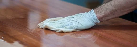 Person trägt Lack auf Holztisch auf